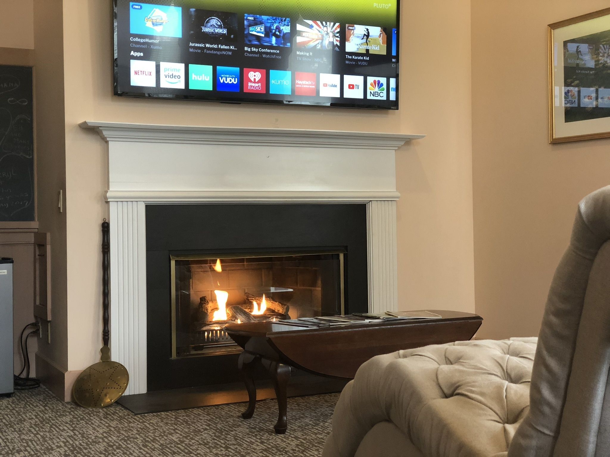 Uma sala de estar com lareira, uma televisão de tela plana montada acima e uma poltrona confortável.