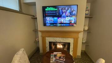 A living room with a flat-screen TV mounted above a fireplace, displaying a TV show.