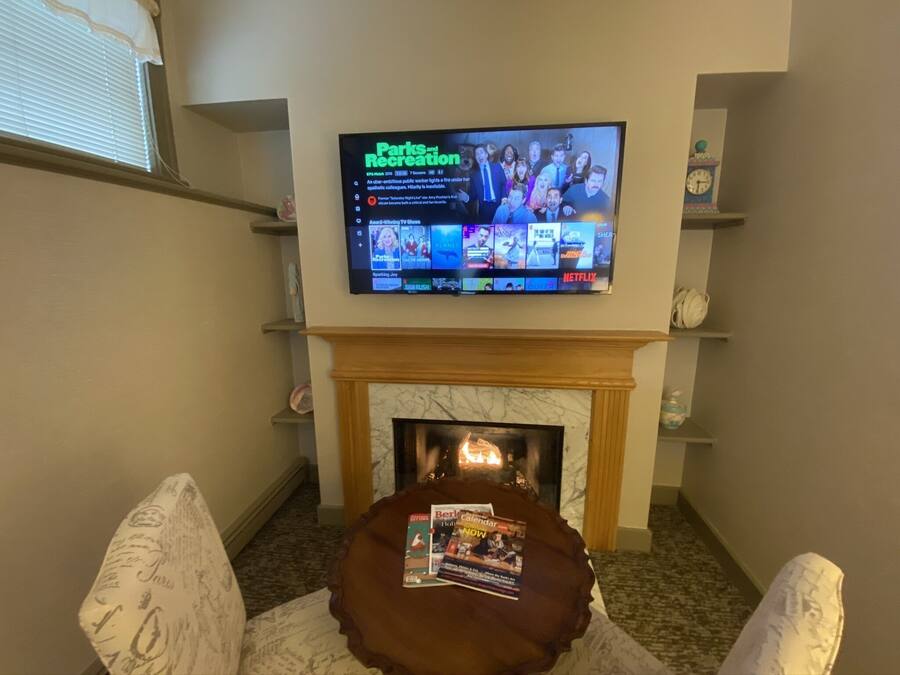 A living room with a flat-screen TV mounted above a fireplace, displaying a TV show.
