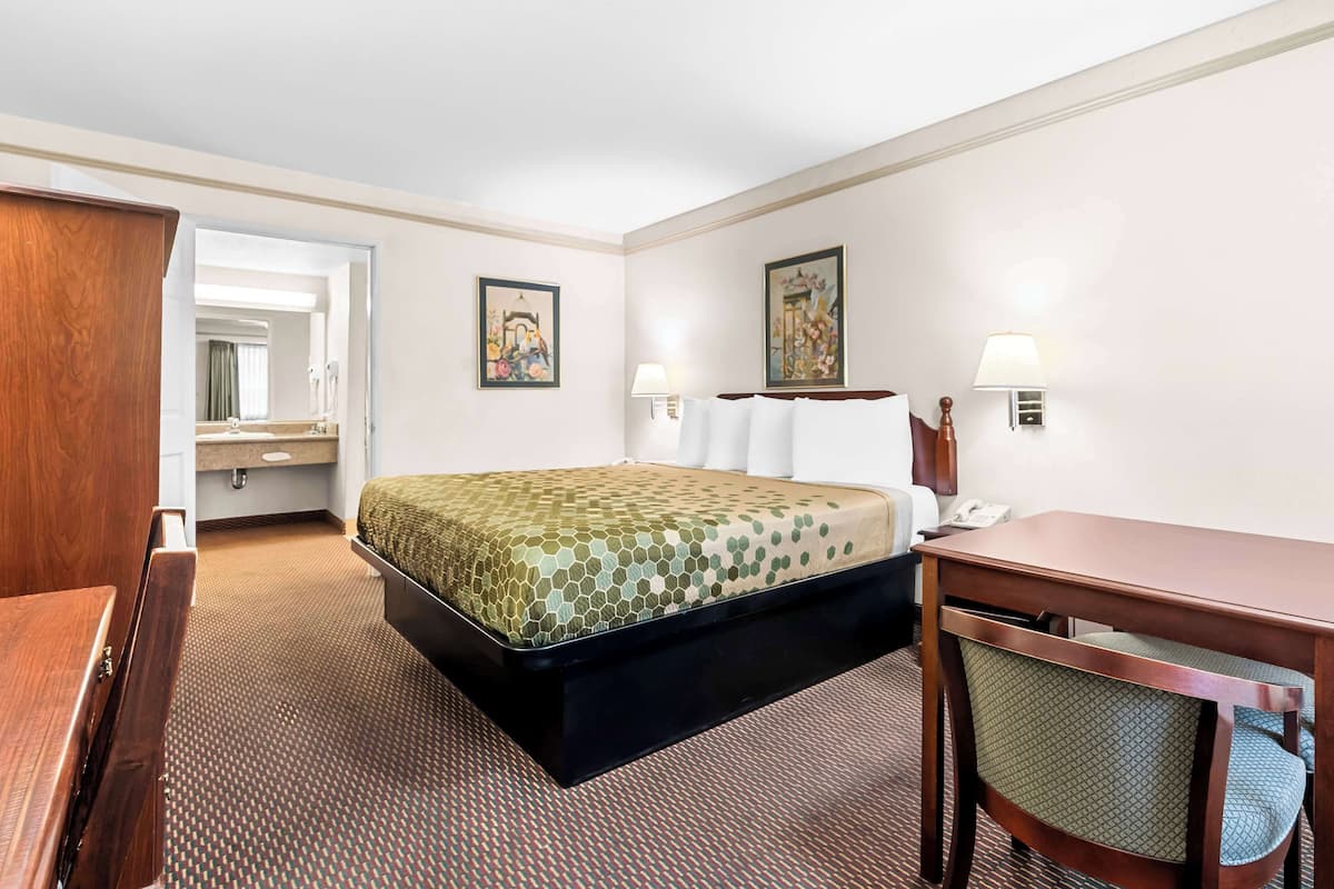 Habitación de hotel con cama, escritorio, silla y baño visible a través de una puerta abierta.