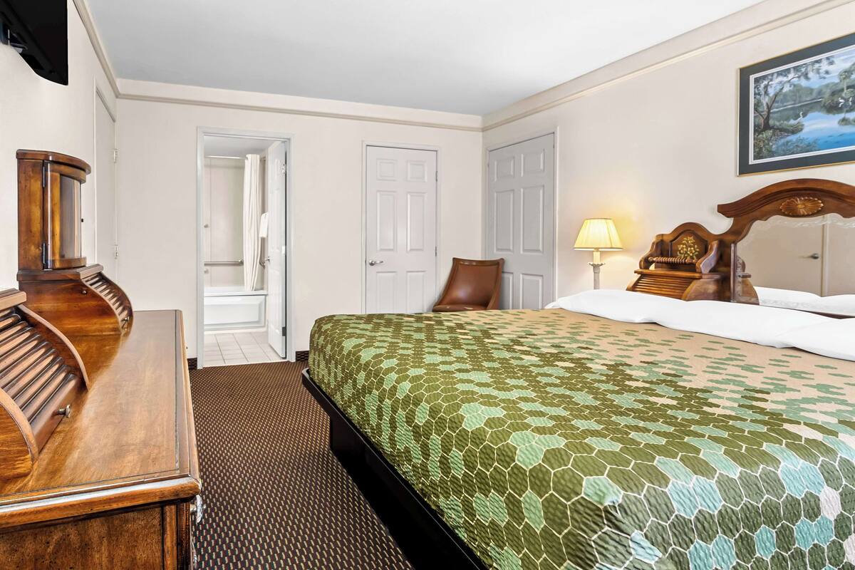 Habitación de hotel con cama, escritorio de madera, lámpara y un cuadro en la pared.