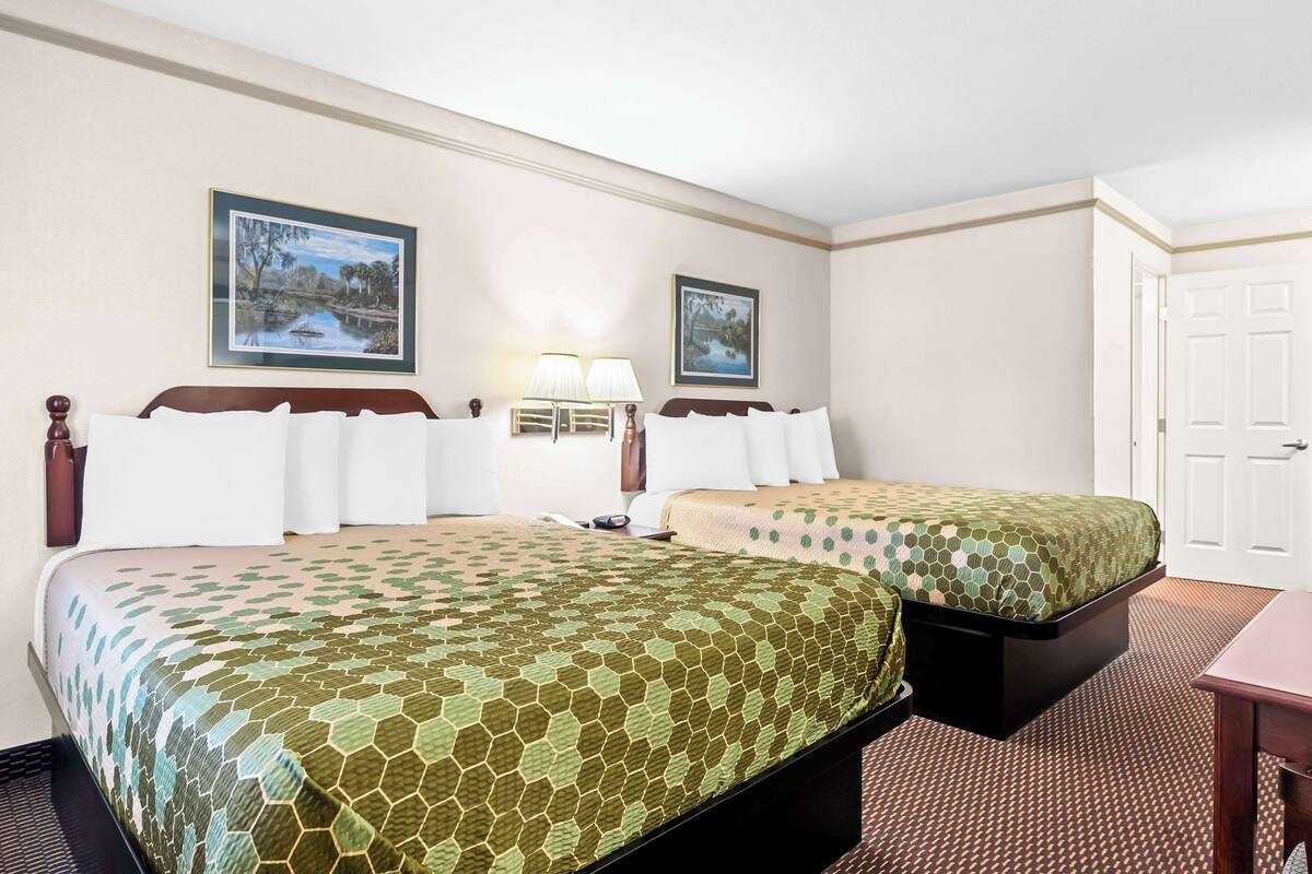 Una habitación de hotel con dos camas, una mesita de noche, una lámpara y dos cuadros en la pared.
