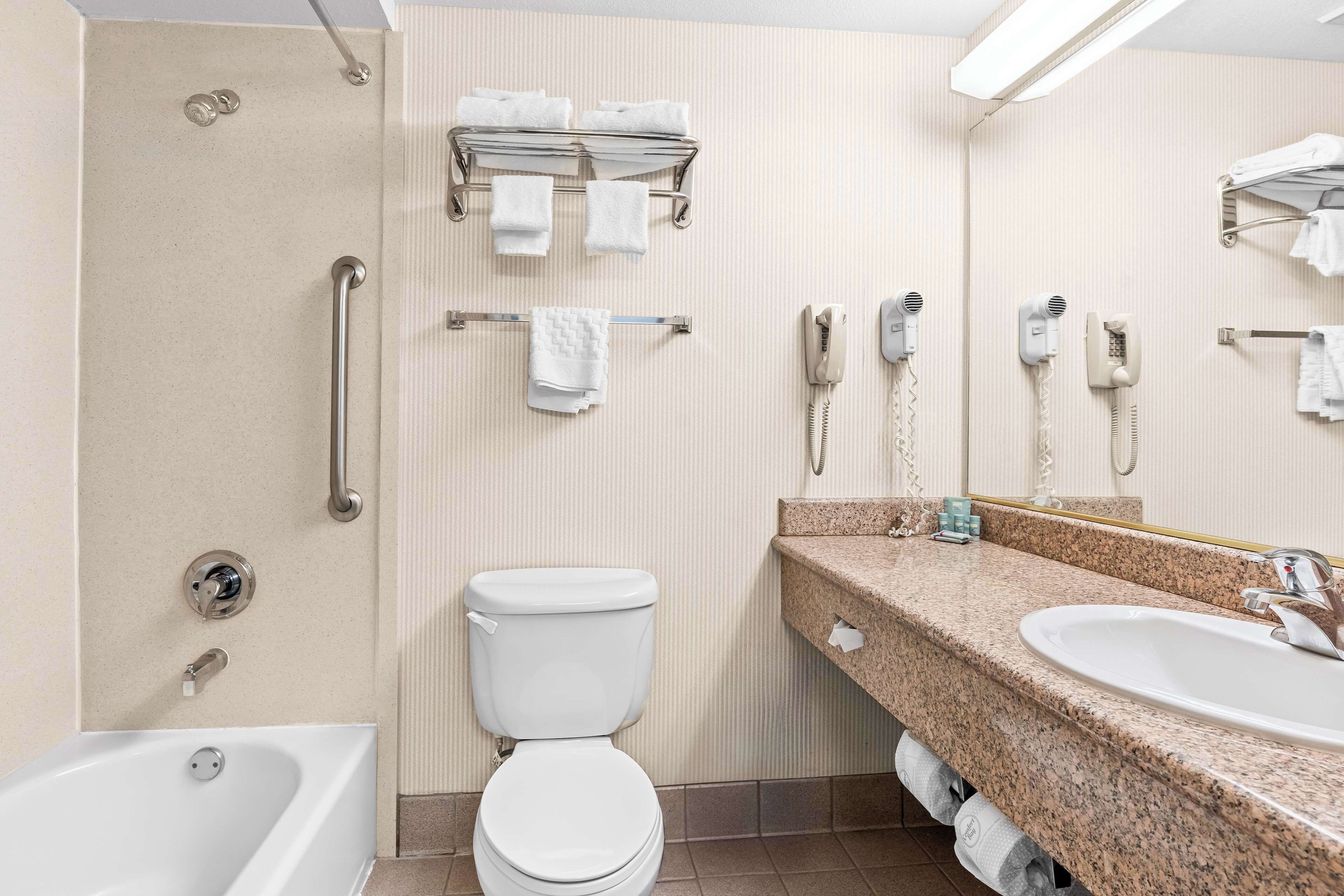 A modern bathroom with a bathtub, toilet, and sink. There are towels and a hairdryer on the wall.