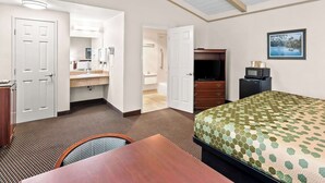 Een hotelkamer met een bed, bureau, stoel, dressoir, televisie en een badkamer zichtbaar door een open deur.