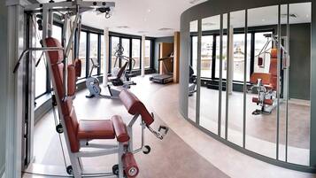 Une salle de sport moderne dotée de divers équipements d’exercice, de grandes fenêtres offrant une vue sur la ville et d’un plafond aux lignes courbes.
