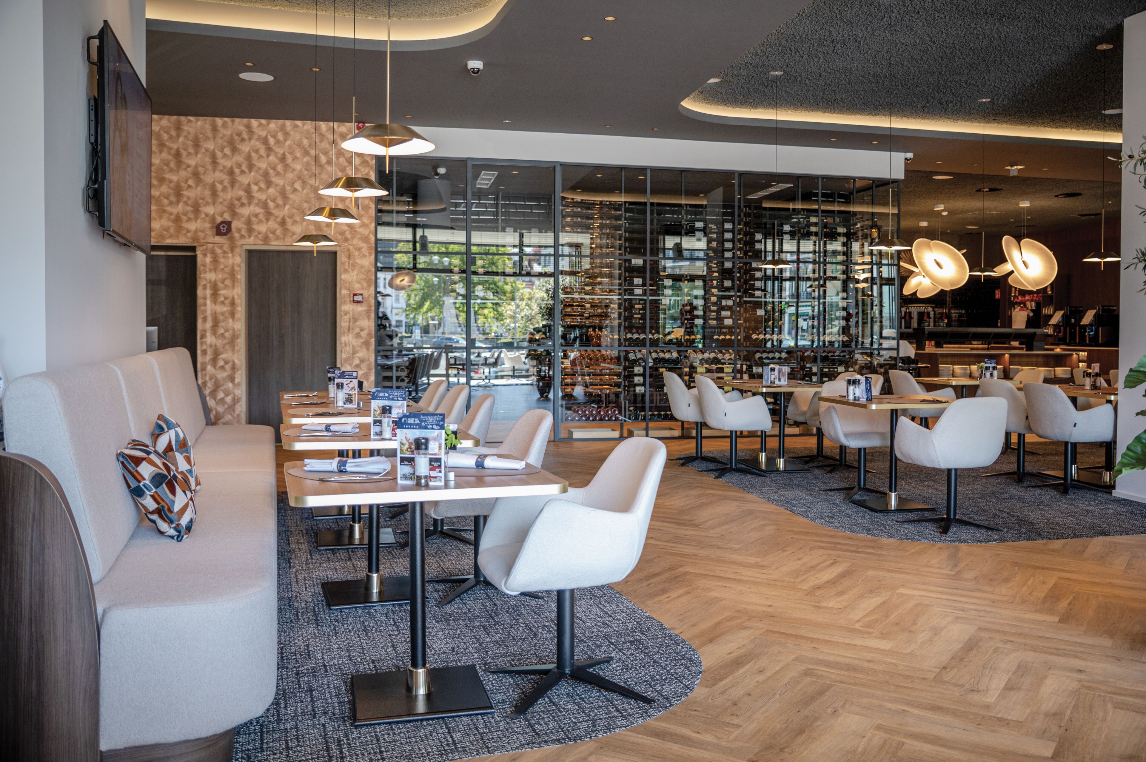 Un moderno vestíbulo de hotel con área de estar, mesas y una exhibición de vinos.