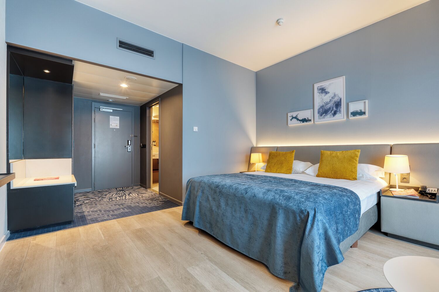 Een moderne hotelkamer met een bed, nachtkastjes, een bureau en een deur naar een badkamer.
