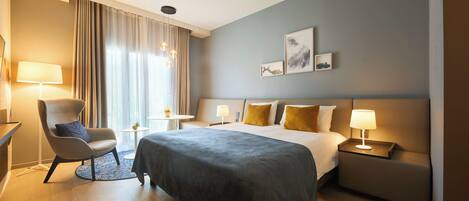 A hotel room with a bed, a chair, a bedside table, a lamp, and a window with curtains.