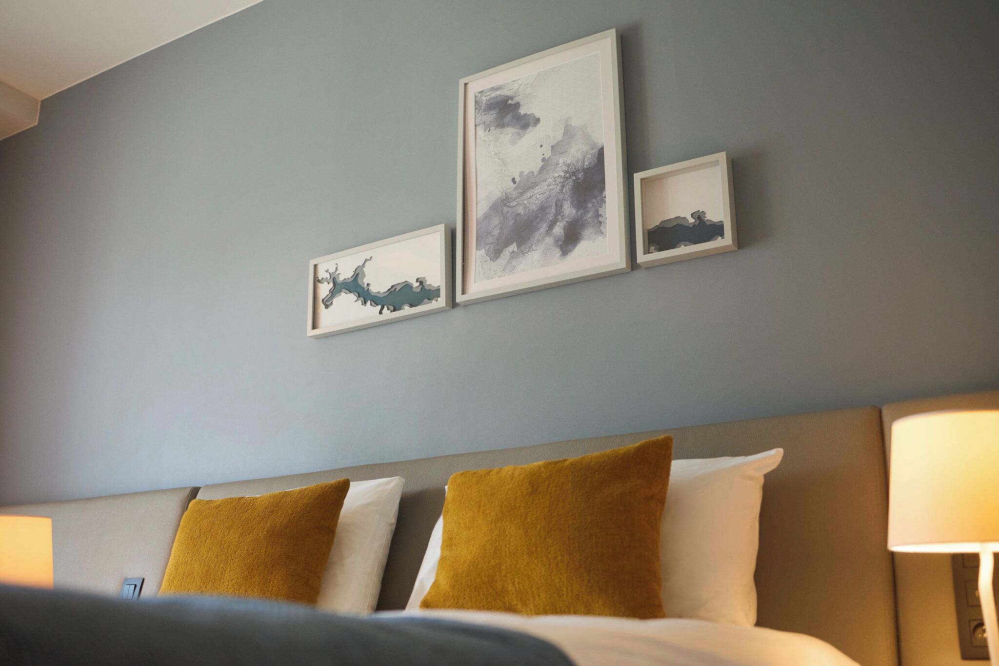 A hotel room with a bed, two pillows, a nightstand, and wall-mounted artwork.