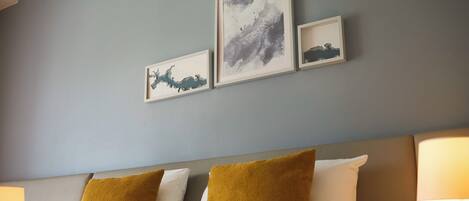 A hotel room with a bed, two pillows, a nightstand, and wall-mounted artwork.