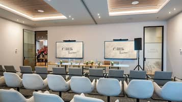 Un salón de conferencias con filas de sillas, una mesa con computadoras portátiles y dos pantallas mostrando 'Welcome to Van der Valk Hotel Spa'.