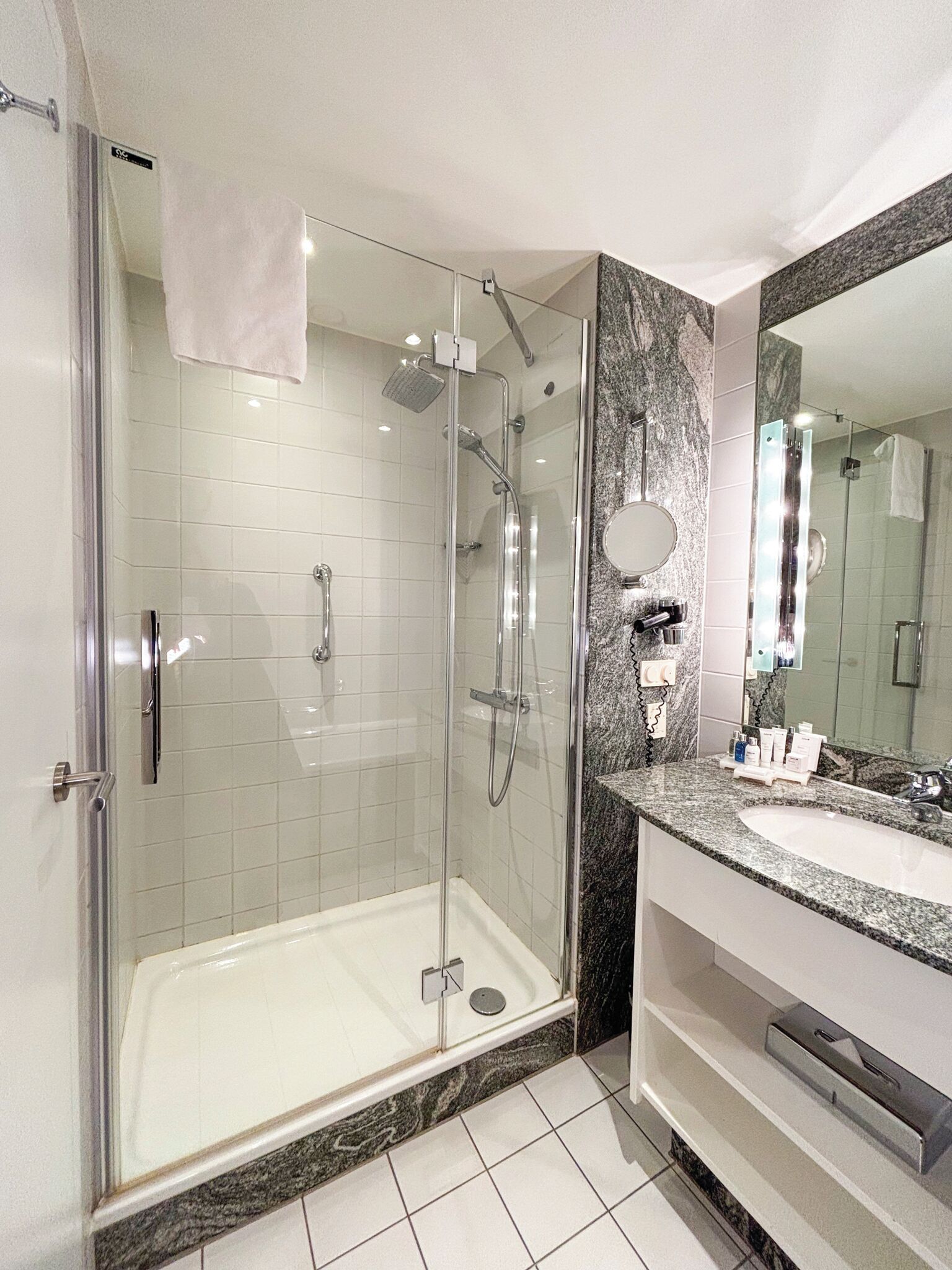 A modern bathroom with a glass-enclosed shower, a marble countertop, and a large mirror.