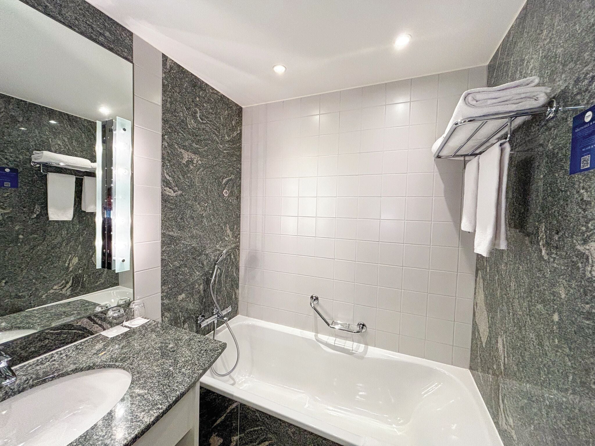 A modern bathroom with a marble sink, a large mirror, a bathtub, and white tiled walls.