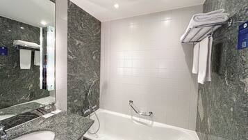 Une salle de bain moderne avec un lavabo en marbre, un grand miroir, une baignoire et des murs recouverts de carreaux blancs.