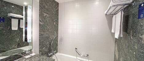 A modern bathroom with a marble sink, a large mirror, a bathtub, and white tiled walls.