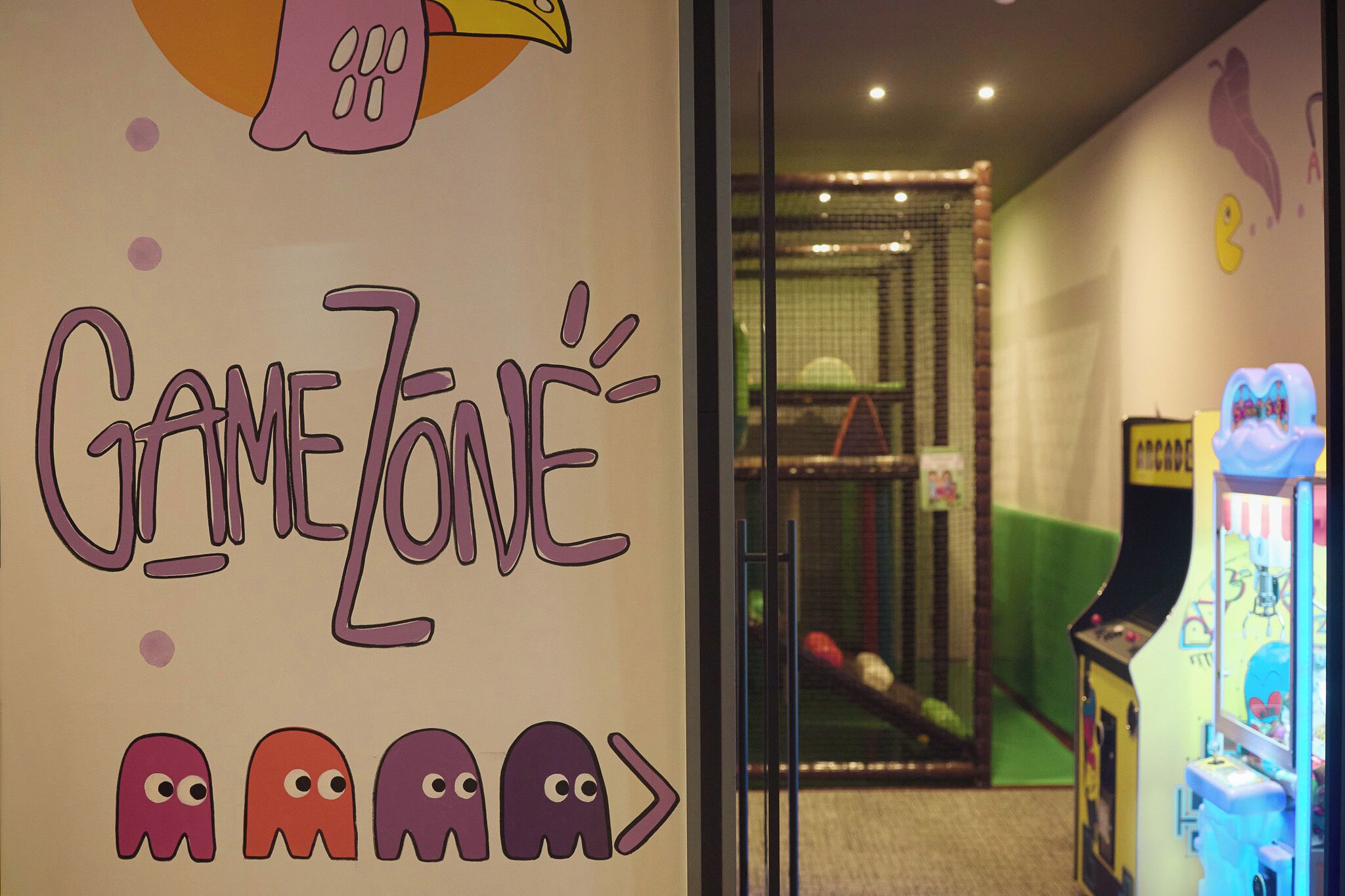 A room with a wall sign reading 'GAMEZONE' and a glimpse of a play area with a green floor and a climbing net.