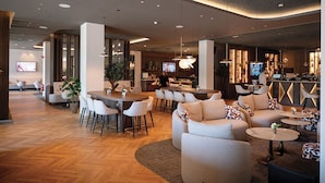 A modern hotel lobby with a bar area, seating arrangements, and a television screen. - Van der Valk Hotel Spa (Spa)