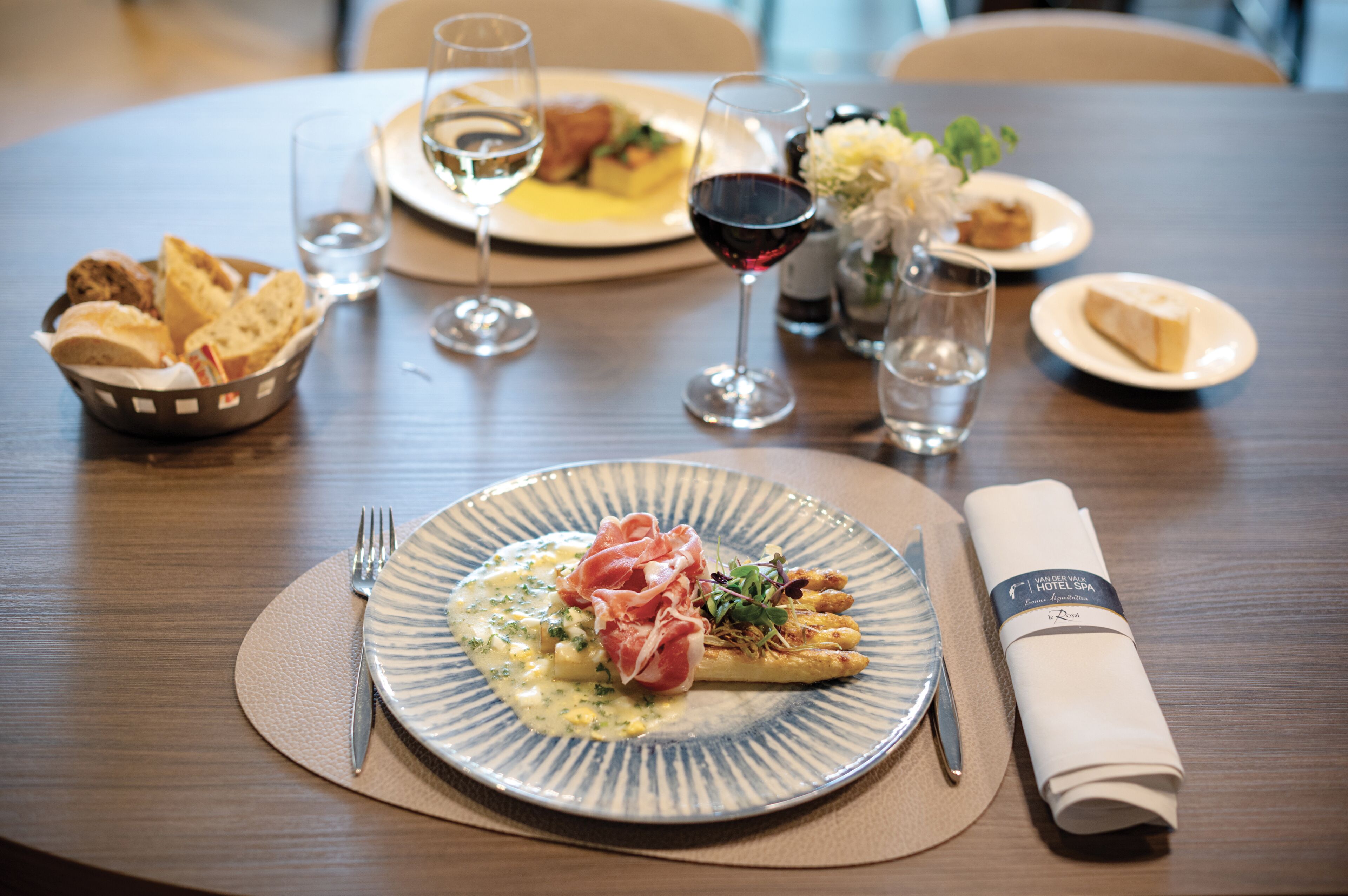 A dining table with plates of food, glasses of wine, and a folded napkin.