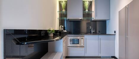 A modern kitchen with a black countertop, stainless steel appliances, and glass shelving.
