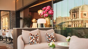 A modern hotel lobby with a sofa, decorative pillows, a vase with flowers, and a view of a historic building through large windows. - Van der Valk Hotel Spa (Spa)