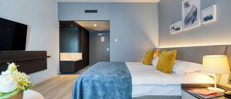 A modern hotel room with a large bed, bedside tables, a flat-screen TV, and artwork on the walls.