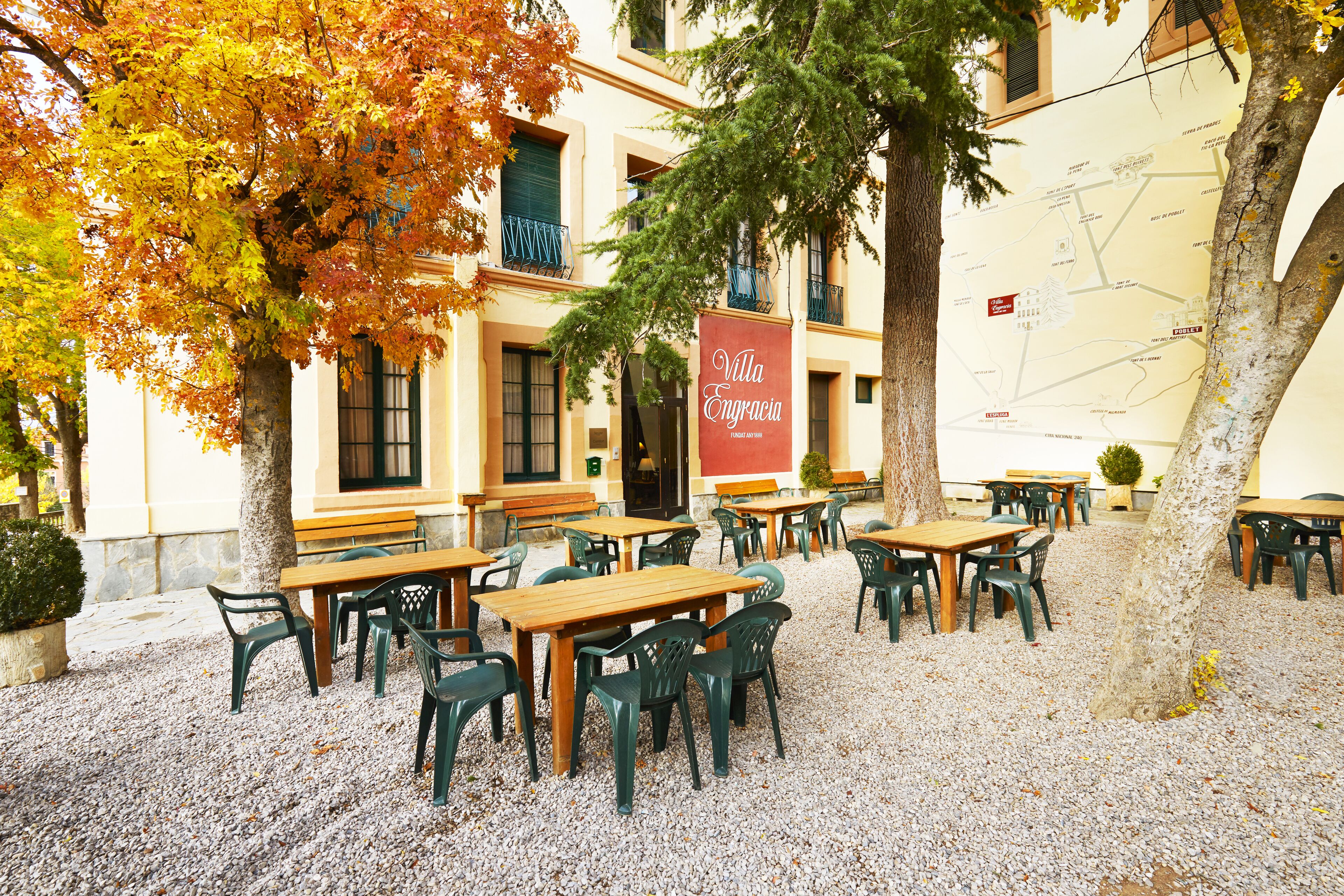 Een terras met tafels en stoelen, een bord met Villa Engroscia en bomen met herfstbladeren.