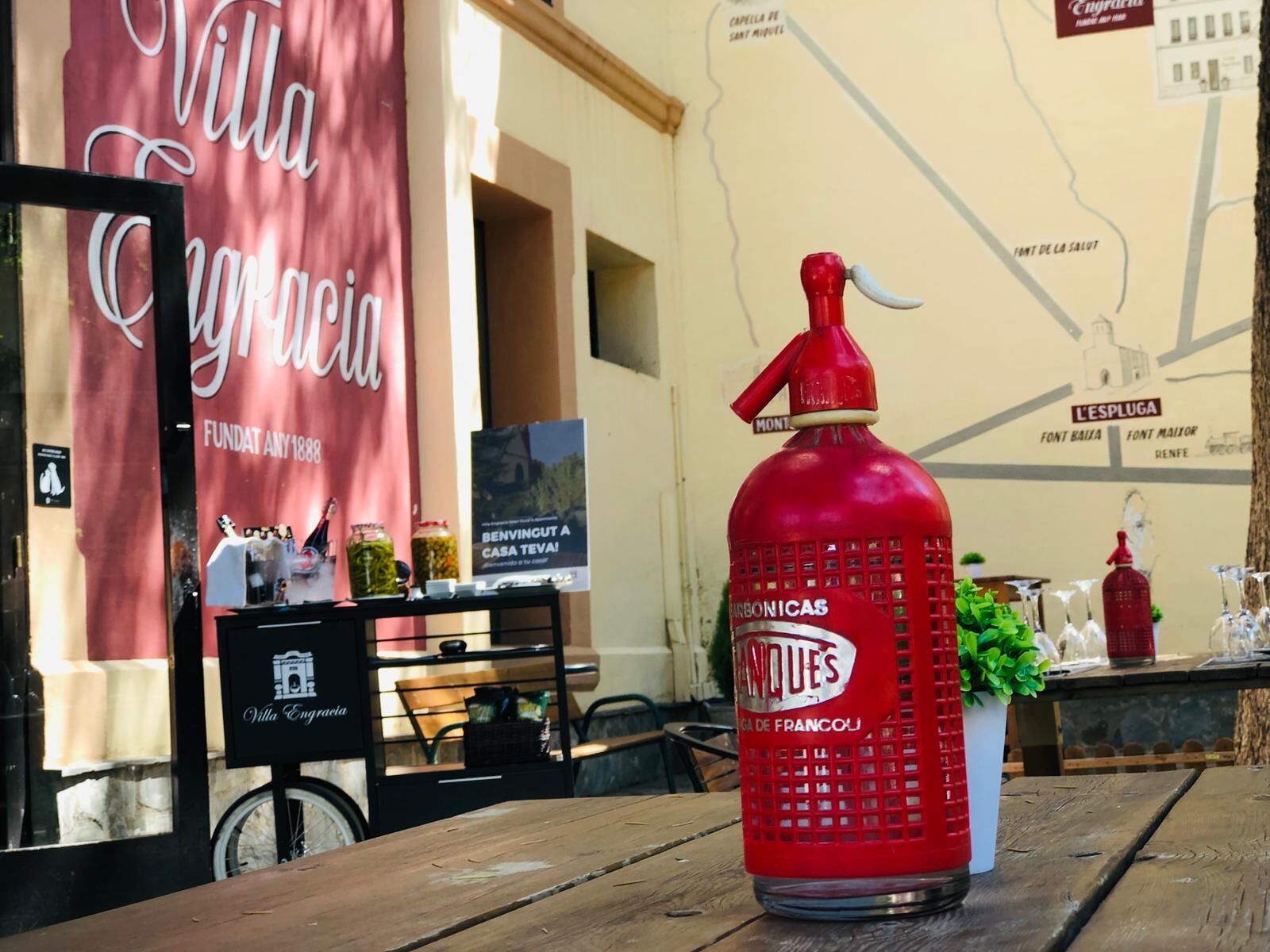 A red gas bottle labeled "FRANQUES" on a wooden table in a restaurant setting.