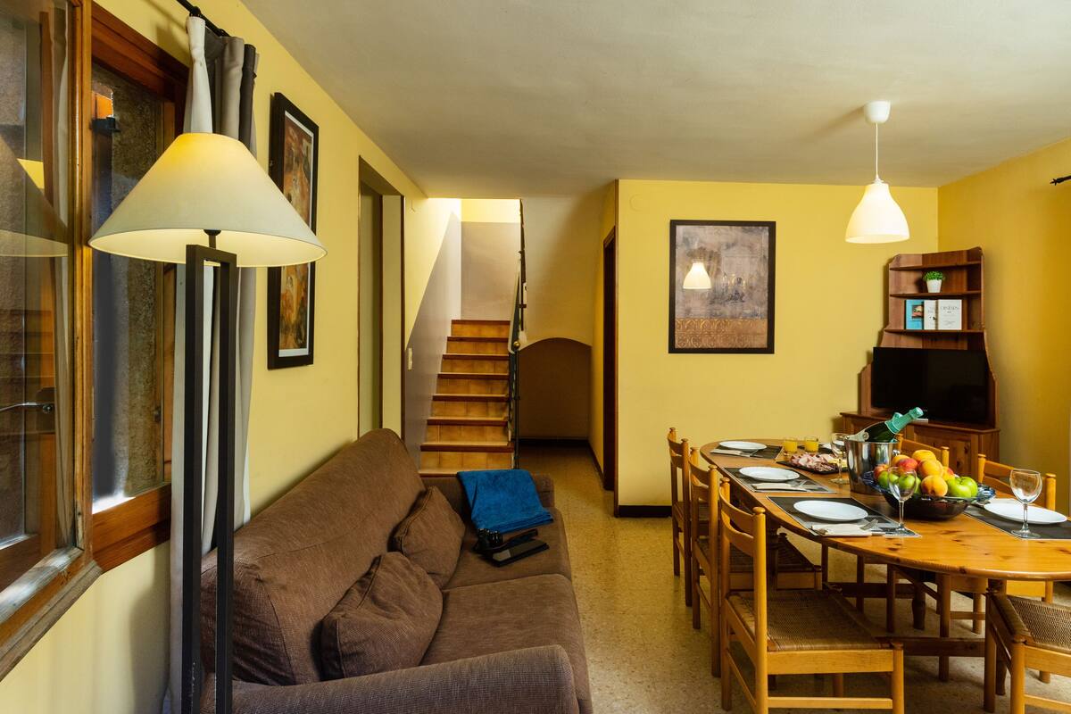 Een eethoek met een houten tafel voor vier personen, een bruine bank en een trap naar een hoger gelegen verdieping.
