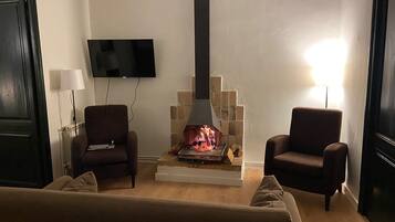 En stue med pejs, to lænestole, en sofa, et fjernsyn ophængt på væggen og en lampe.