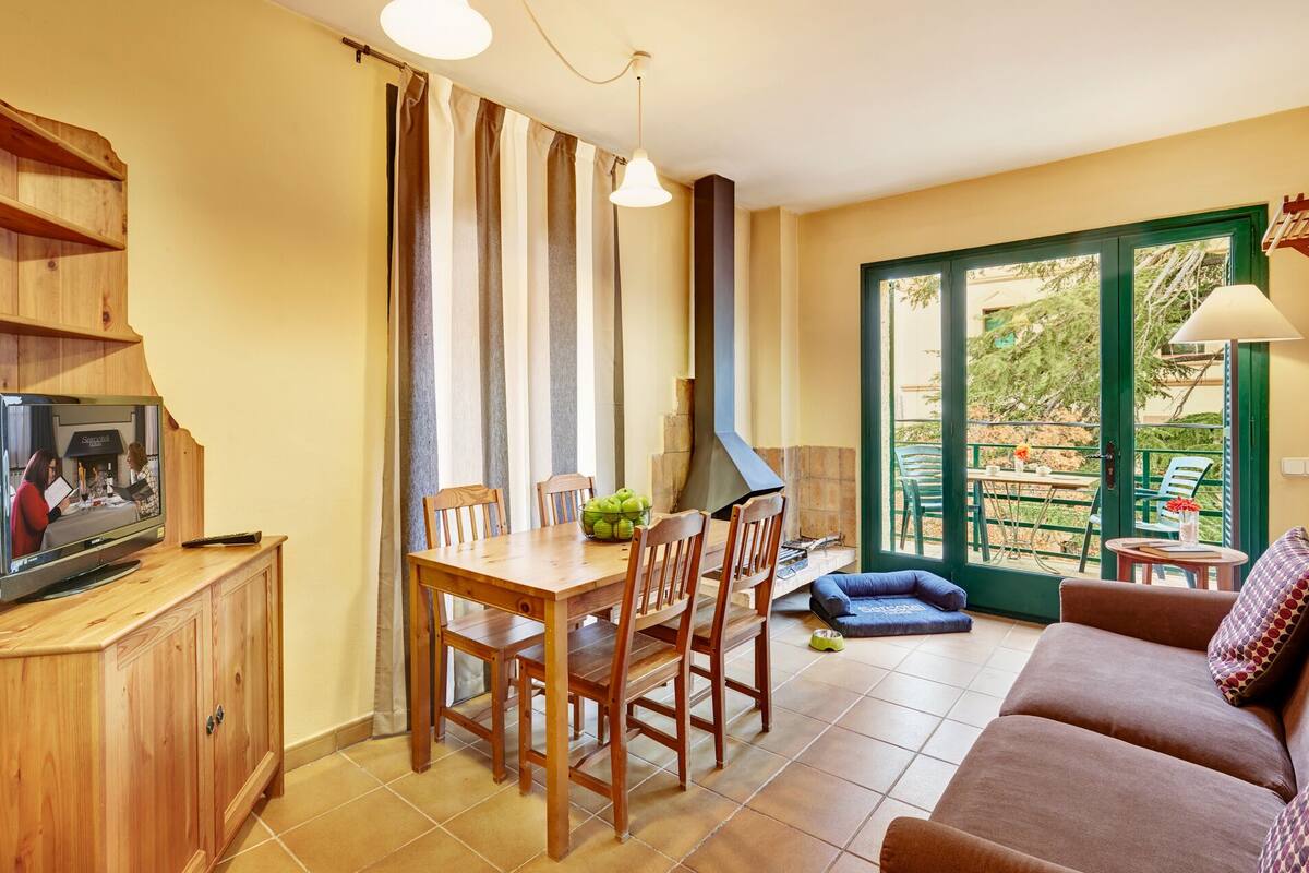 Een gezellige woonkamer met een houten tv-meubel, een eettafel met stoelen, een bank en een schuifpui naar een buitenruimte.