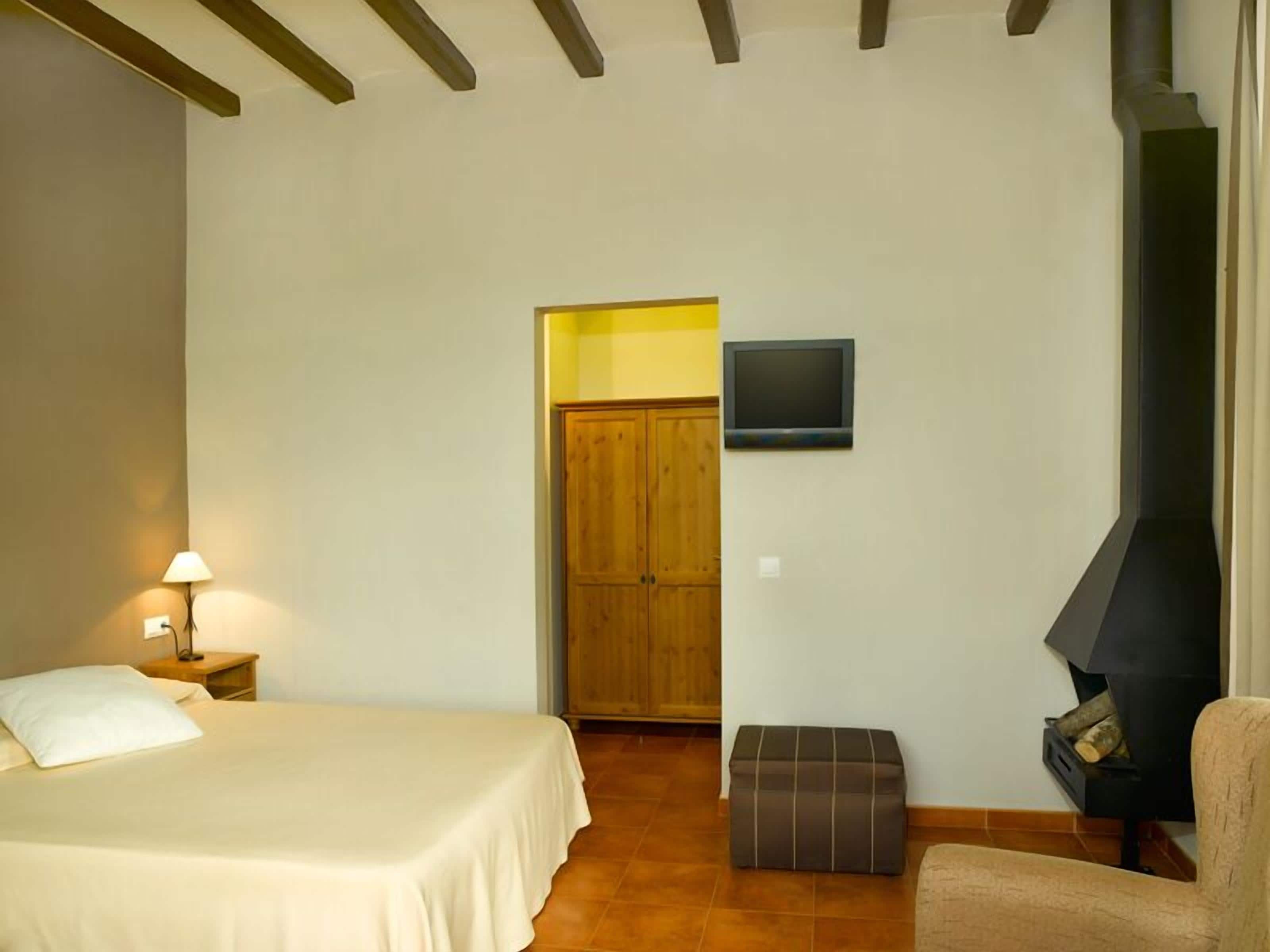 A bedroom with a bed, a nightstand, a TV, a fireplace, and a wooden door.