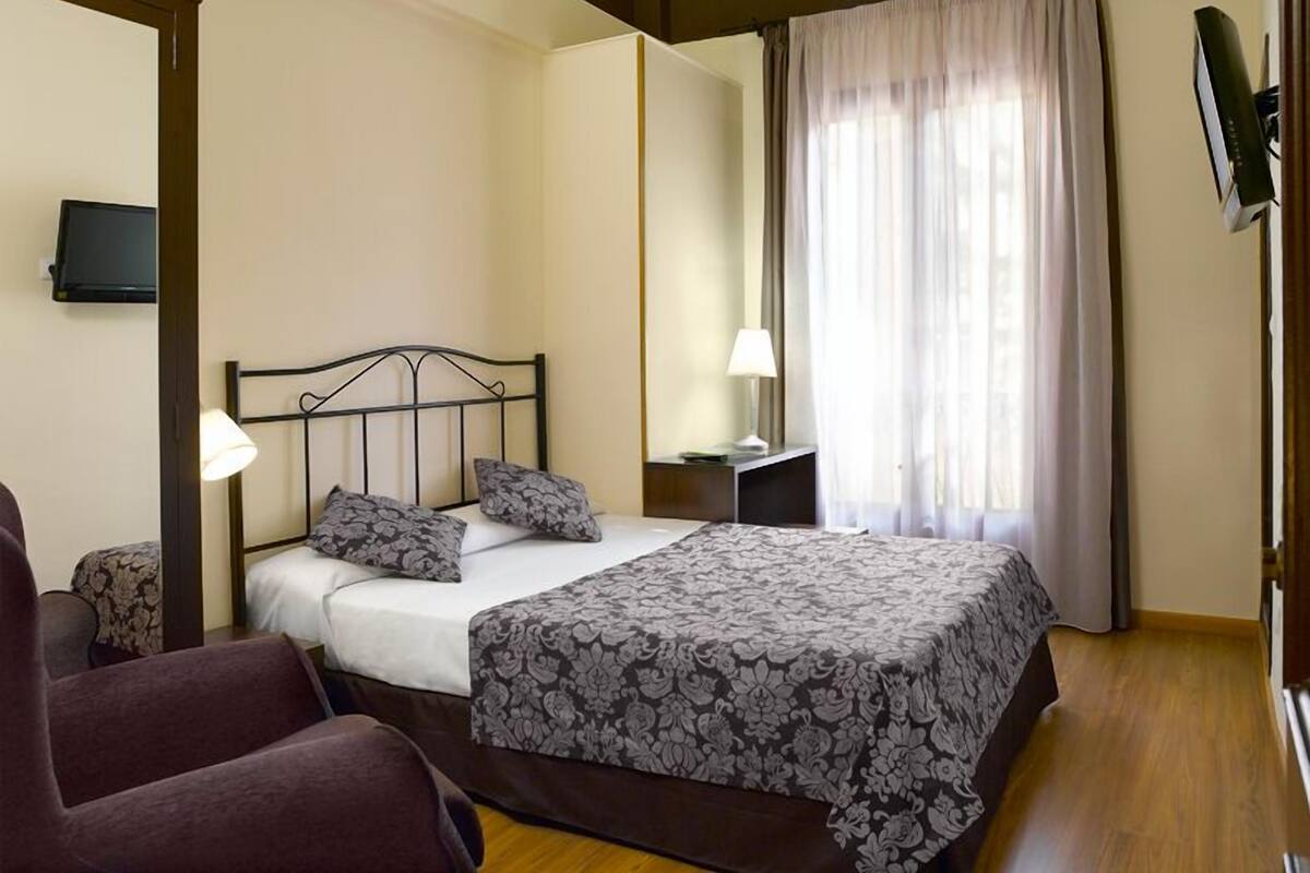 Een slaapkamer met een bed, twee bedlampen, een televisie aan de muur en een stoel.
