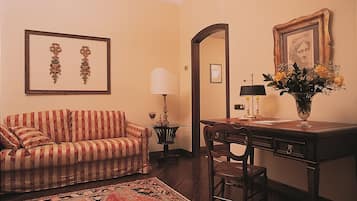 A room with a striped sofa, a desk with a lamp, a vase with flowers, and framed pictures on the wall.