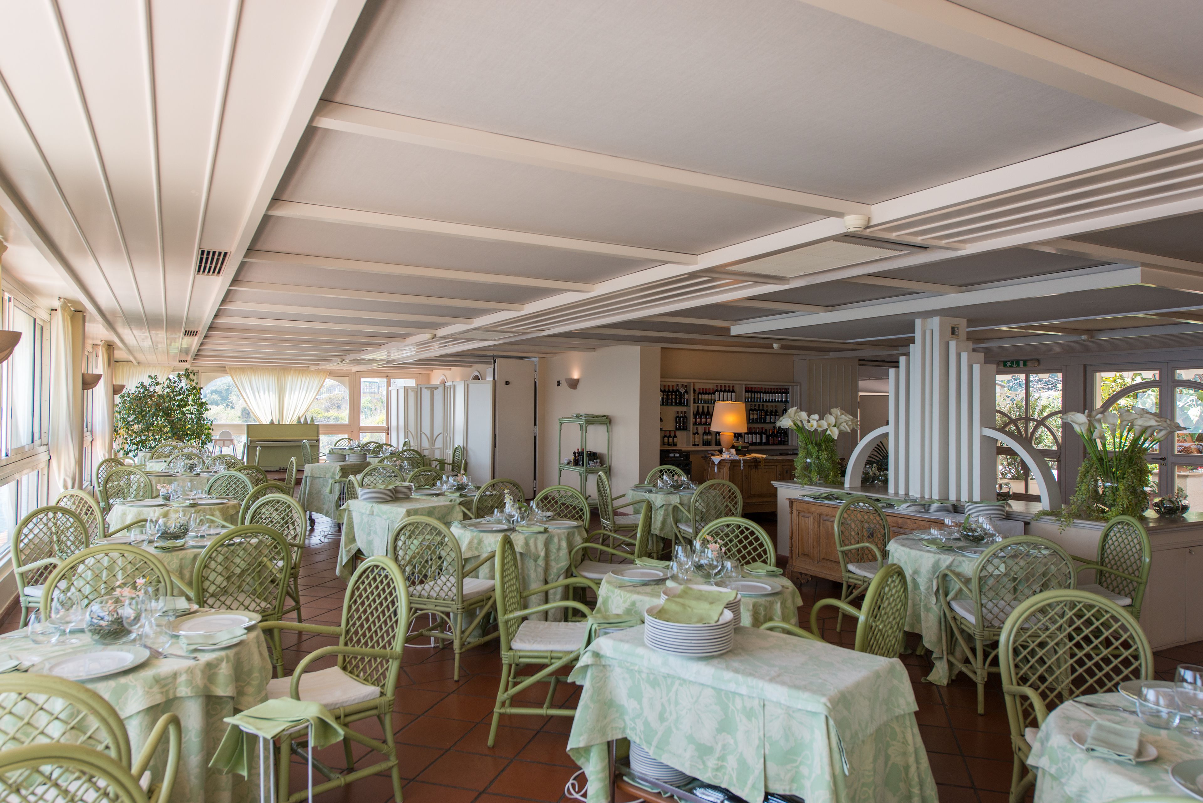 Un restaurant doté de nombreuses tables et chaises, d’un plafond orné de motifs linéaires et offrant une vue sur l’extérieur grâce à de grandes fenêtres.