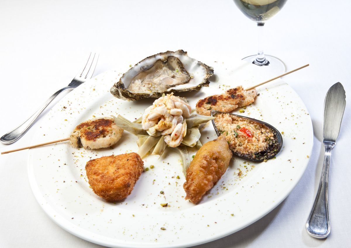 A plate of seafood including oysters, shrimp, and breaded items, with a fork and knife on the side.