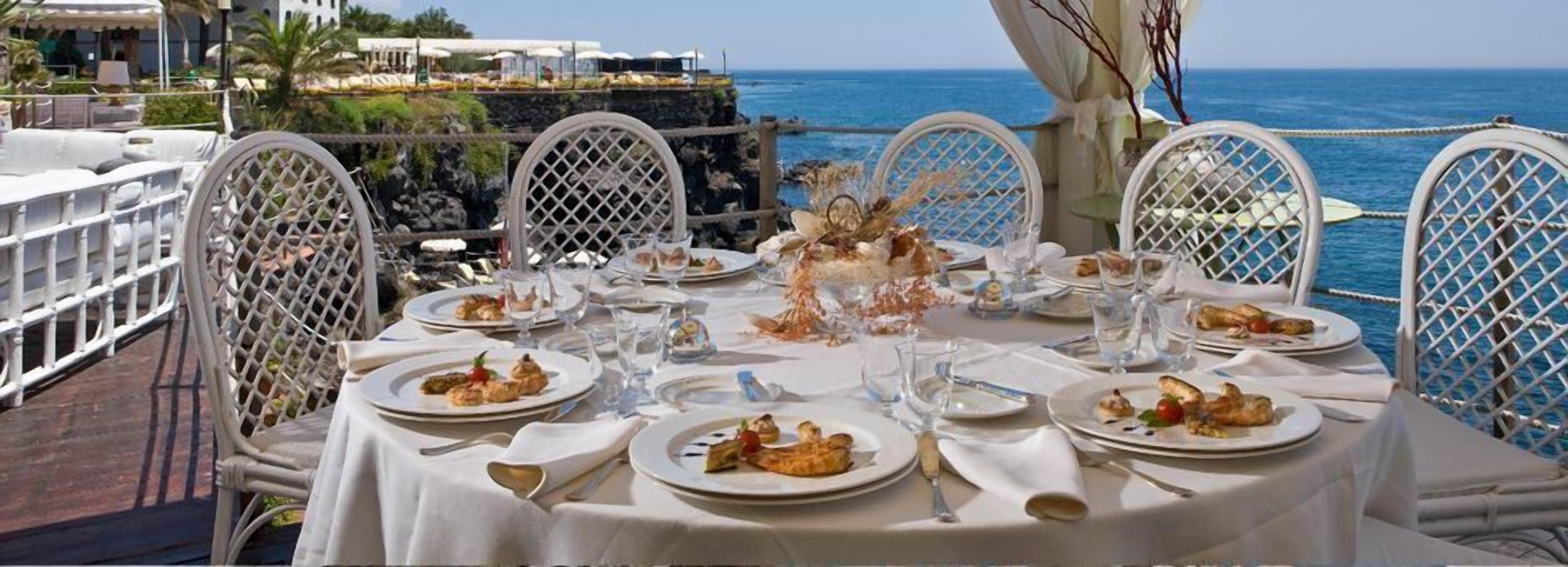 Une table dressée pour un repas, avec des assiettes remplies de nourriture, des verres et des couverts, donnant sur une étendue d’eau.