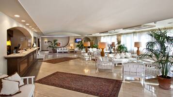 Un'ampia hall dell'hotel con reception, zone salotto e uno schermo televisivo.
