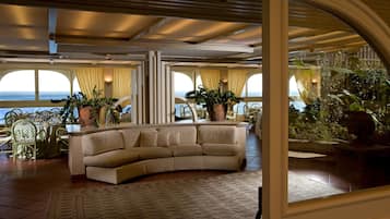 A luxurious living room with a curved sofa, large windows, and potted plants.