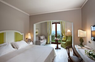 Une chambre d’hôtel dotée d’un grand lit, d’un coin salon avec une table et des chaises, d’un balcon avec vue et d’un téléviseur fixé au mur.