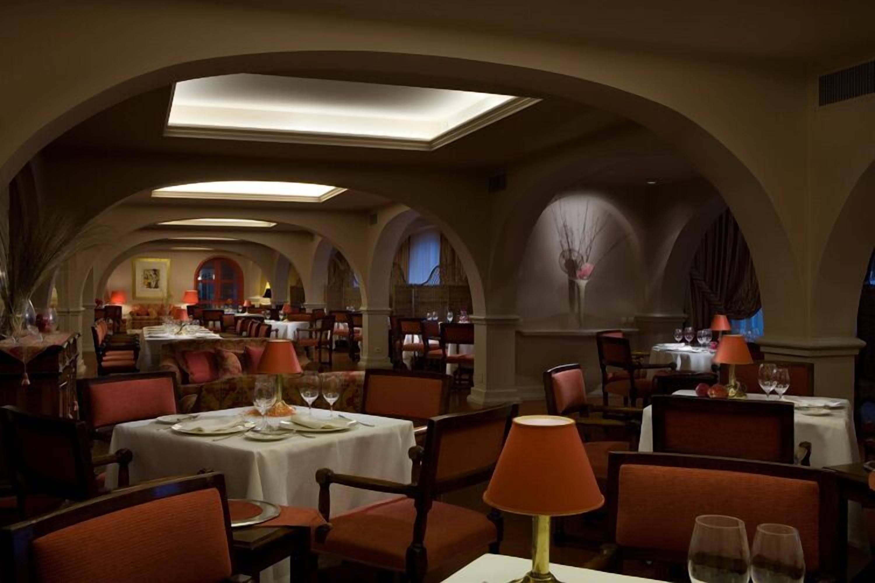 A restaurant with multiple tables and chairs, arched ceilings, and warm lighting.
