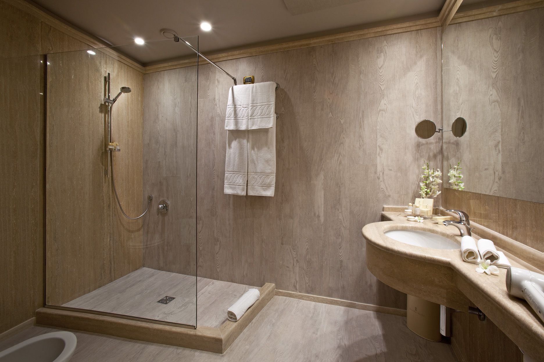 A modern bathroom with a glass-enclosed shower, a wooden vanity with a sink, and a mirror.