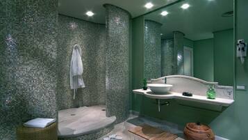 A bathroom with a mosaic tile wall, a white sink, a mirror, and a shower area.