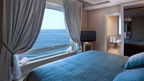 Habitación de hotel con una cama grande, un televisor sobre una mesita y vista al mar por la ventana.