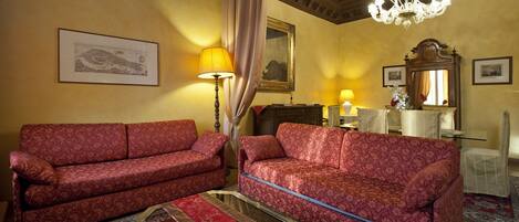 A room with two red patterned sofas, a chandelier, a mirror, and a table with a lamp.