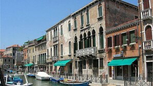 Un canal con barcos amarrados a lo largo de sus orillas, rodeado de edificios históricos con ventanas arqueadas y balcones.