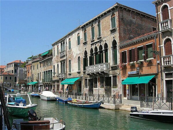 A canal with boats docked along the sides, surrounded by historic buildings with arched windows and balconies.