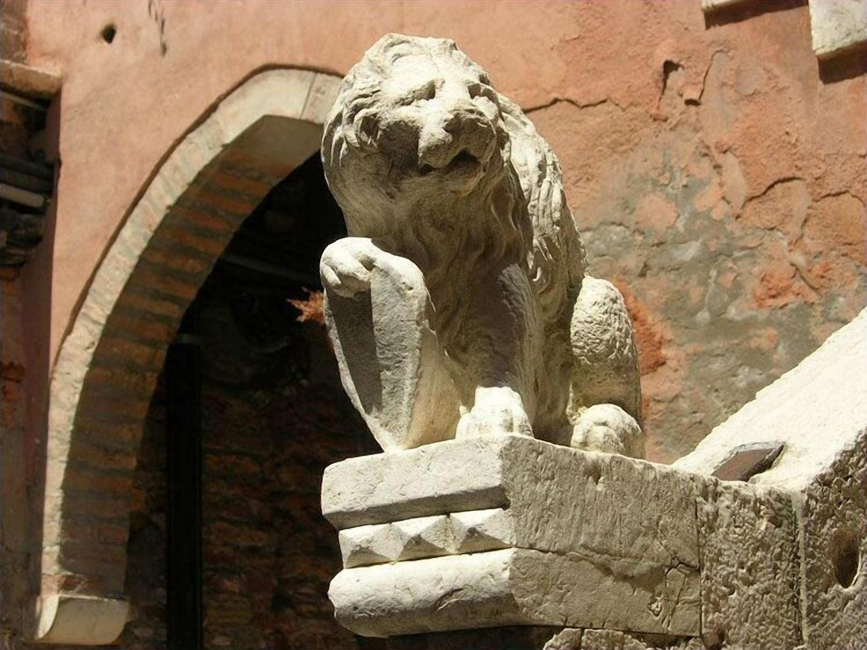 A stone lion statue on a ledge with an arched doorway in the background.