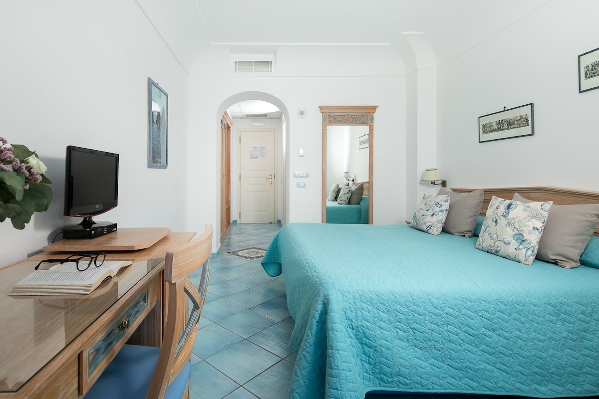 A bedroom with a bed, a desk with a computer, and a mirror.