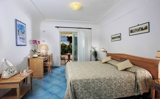 Habitación de hotel con cama, escritorio, silla, lámpara y vistas al exterior.