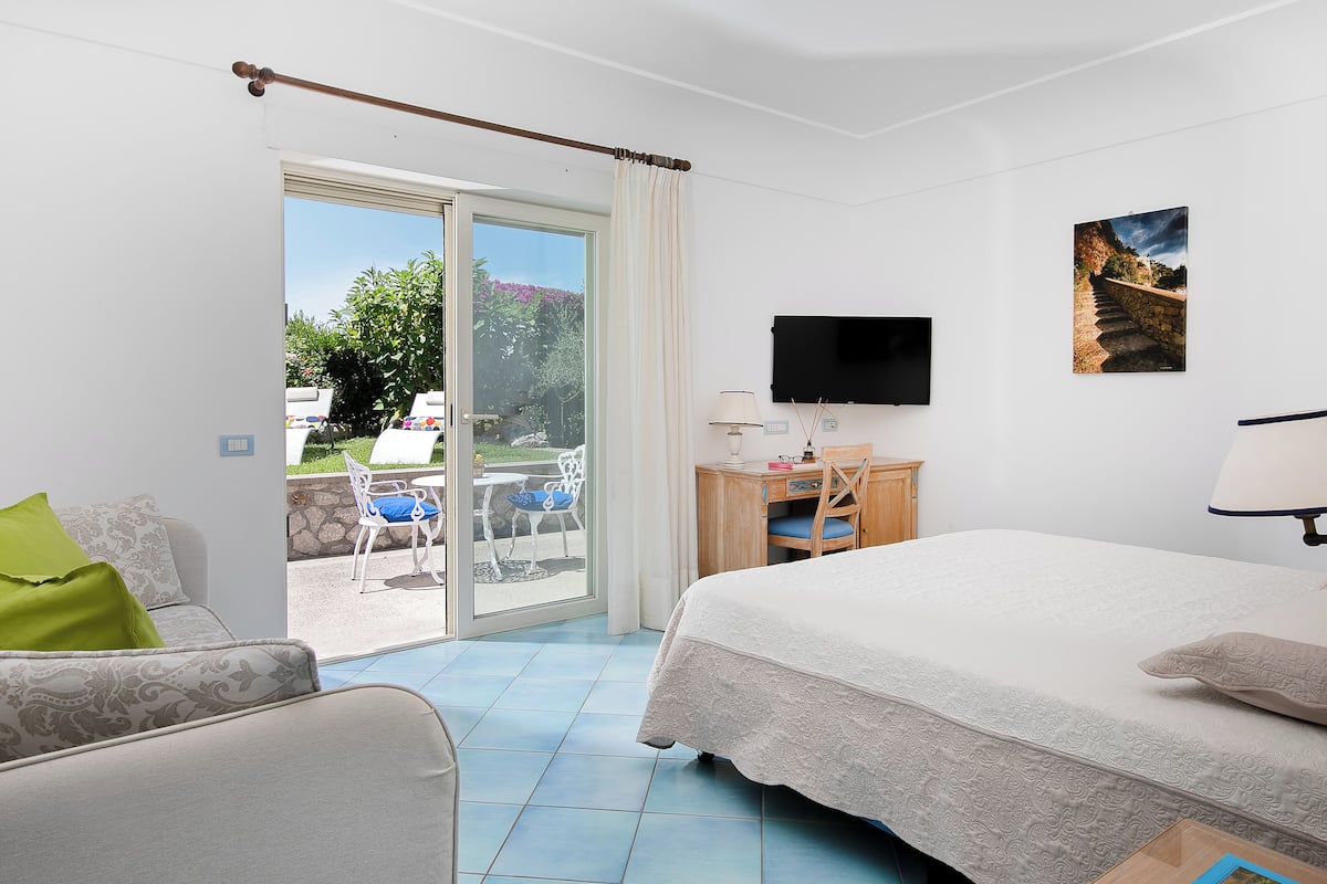 A hotel room with a bed, a desk, a TV, and a sliding glass door to an outdoor area with a table and chairs.